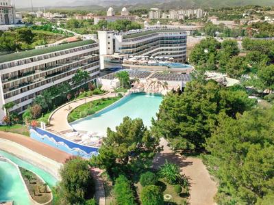 Large hotel with multiple buildings, a big pool, and abundant greenery surrounding it.