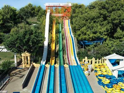 Kolorowe zjeżdżalnie wodne wielopasmowe w parku wodnym otoczone zielonymi drzewami i parasolami.