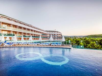 Hotel with large infinity pool overlooking green landscape at sunset.