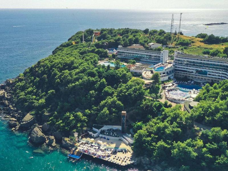 Kompleks hotelowy na zielonym półwyspie nad niebieskim morzem z wieloma budynkami i plażą.