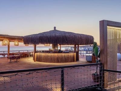 Atmosfera serale in un elegante bar sulla spiaggia con tetto di paglia e posti a sedere su un molo di legno.