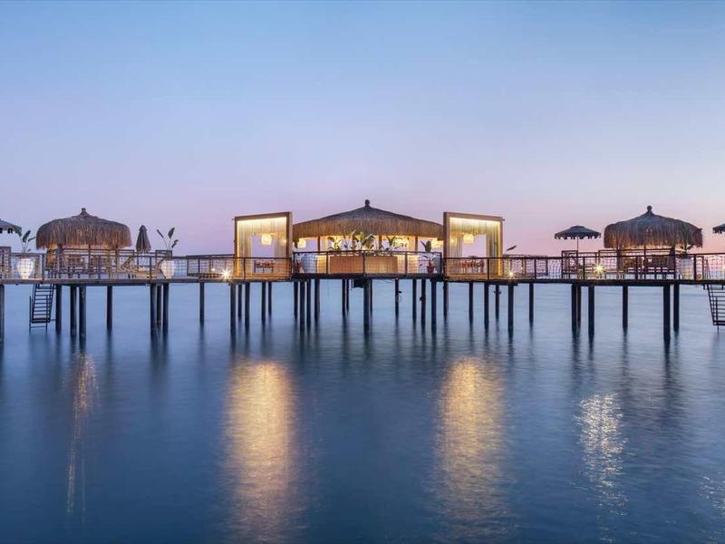 Bungalow costruiti sull'acqua con illuminazione al crepuscolo su mare calmo.