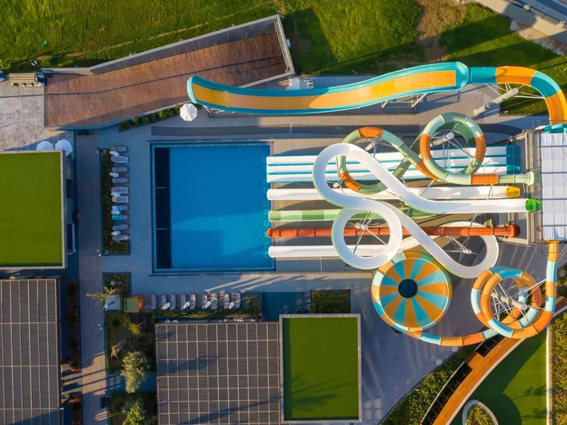 Luftaufnahme von bunten Wasserbahnen mit Schwimmbecken und Grünflächen drumherum.