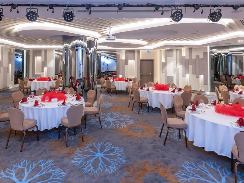 Eleganter Bankettsaal mit runden Tischen, weißen Tischdecken und roten Servietten, modernes Design.