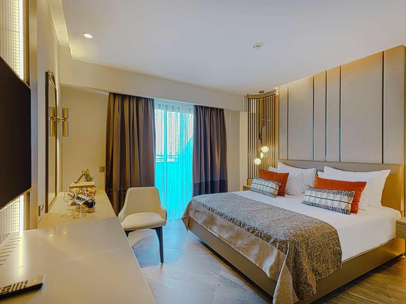 Modernes Hotelzimmer mit großem Doppelbett, bequemen Stühlen und Balkon mit Gebäudeausblick.