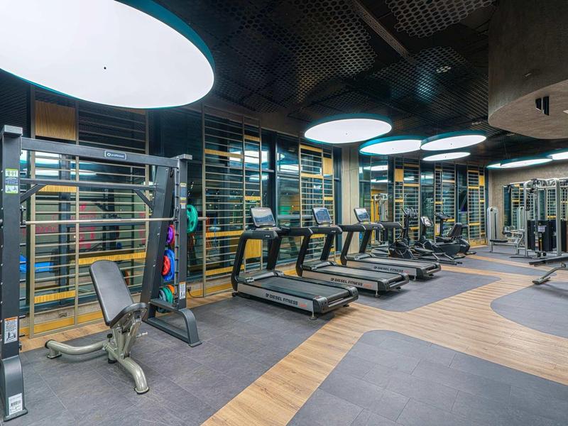 Großer moderner Fitnessraum mit Laufbändern, Kraftgeräten, Holz- und Gummiboden, hellem Deckenlicht.