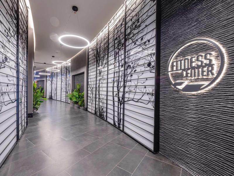 Moderner Flur mit dunklen Böden, beleuchteten Baumgrafiken und Fitnessstudio-Logo an der Wand.