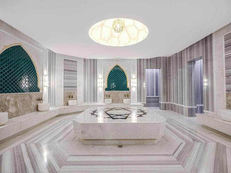 Luxuriöser, symmetrischer Hamam mit Marmorwänden, Einbaubänken, kunstvollen Nischen und zentralem Becken.