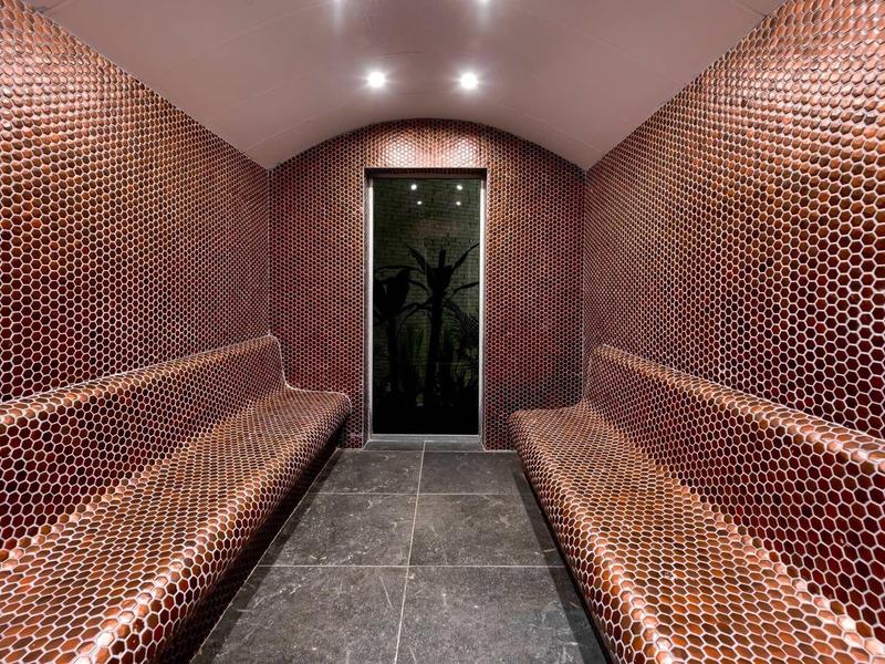 Moderner, rechteckiger Raum mit gewölbter Decke, braunen sechseckigen Fliesen und hellen Einbaustrahlern.