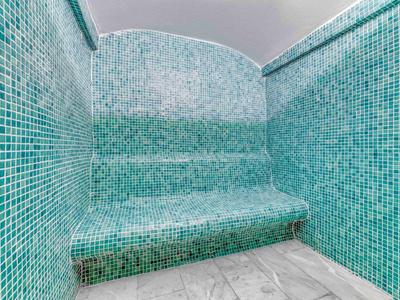 Eine mit türkisfarbenen Mosaikfliesen verkleidete Sitzecke, umgeben von Wänden, mit glattem Marmorboden.