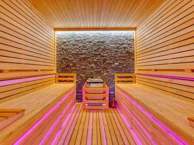Moderne Sauna mit Holzverkleidung, Steinen im Hintergrund und pinkfarbener LED-Beleuchtung unter den Bänken.