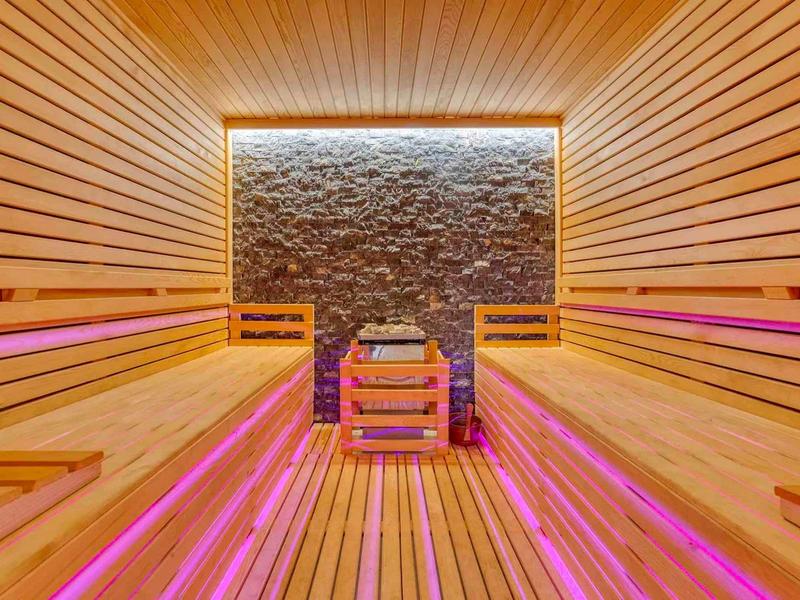 Sauna moderna con pannelli in legno e illuminazione LED rosa lungo le panche.