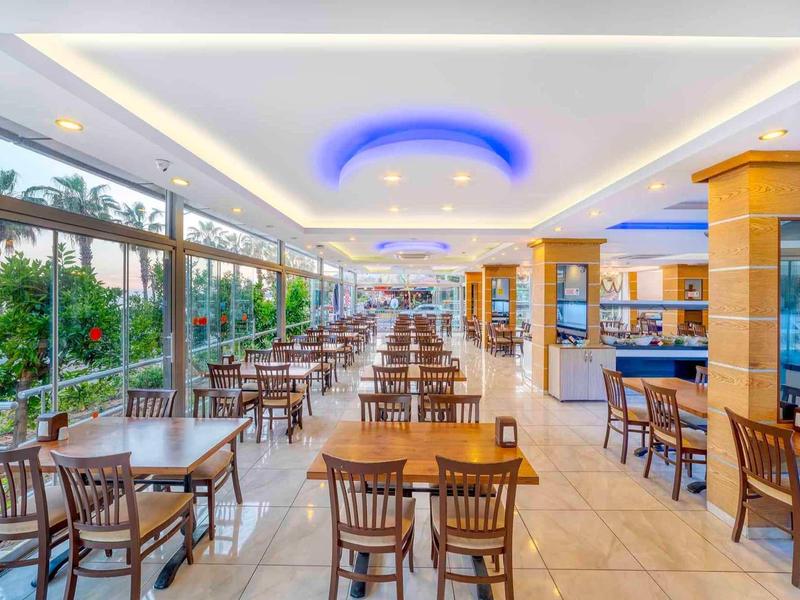 Ristorante moderno luminoso con tavoli e sedie di legno, grandi finestre in vetro e illuminazione blu sul soffitto.
