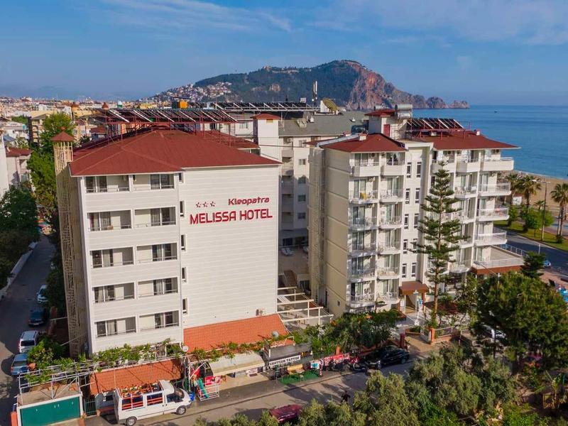 Edificio alberghiero su più piani vicino alla costa con vista montagna e cielo azzurro.