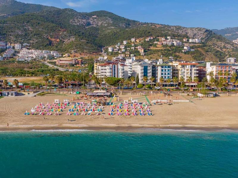 Spiaggia con ombrelloni, sdraio e hotel davanti a una collina boschiva in una giornata limpida.