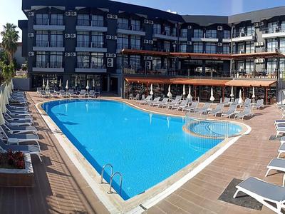 Nowoczesny kompleks hotelowy z dużym basenem na zewnątrz i wieloma leżakami na tarasie.