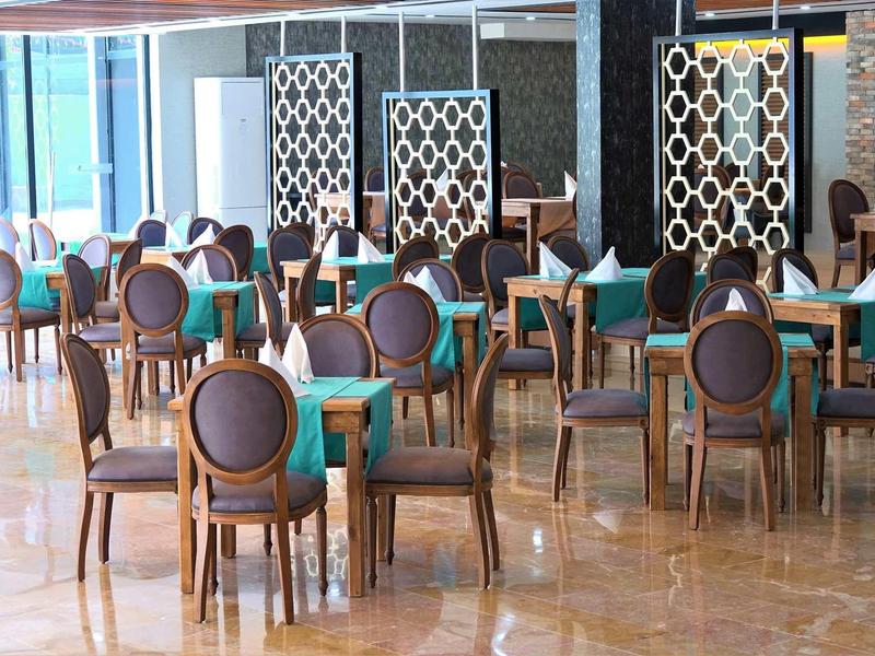 Nowoczesna jadalnia z krzesłami o okrągłych oparciach i stołami z zielonymi obrusami.