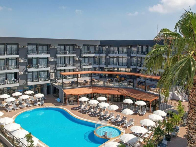 Nowoczesny hotel z dużym basenem, parasolami i palmami pod niebieskim niebem.