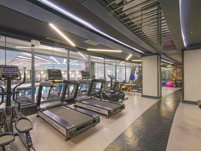 Moderner Fitnessraum mit Laufbändern, Crosstrainern und Kraftgeräten in hellem Ambiente.
