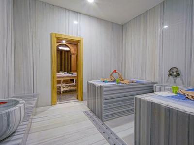 Moderner Wellnessraum mit Sauna, zwei Liegen und Marmorbecken, helle Wände und sanfte Beleuchtung.
