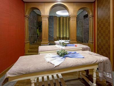 Gemütlicher Wellnessraum mit Massageliege, roten Wänden und dekorativen Vorhängen.