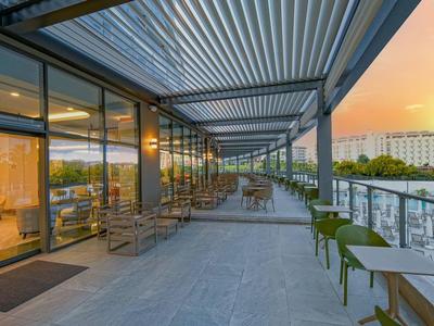 Moderner Balkon mit Glasgeländer, Pflanzen und Blick auf Stadt bei Sonnenuntergang.