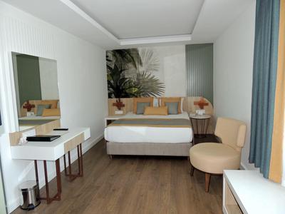 Chambre d'hôtel moderne avec lit double, fauteuil, bureau et décoration élégante dans des tons neutres.