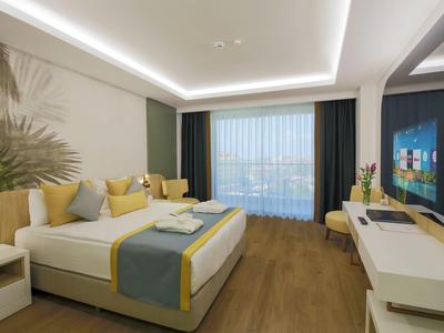 Chambre d'hôtel moderne avec grand lit, sol en bois et fenêtres avec rideaux.