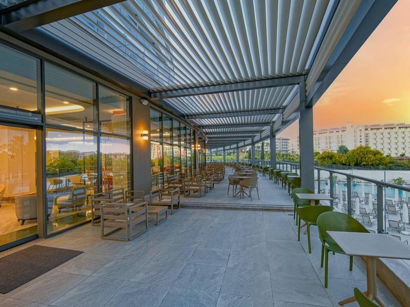 Buitenterras met zitplaatsen met uitzicht op zwembad en water bij zonsondergang.