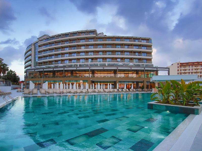 Groot hotel met gebogen balkons boven een turquoise zwembad onder een bewolkte hemel.