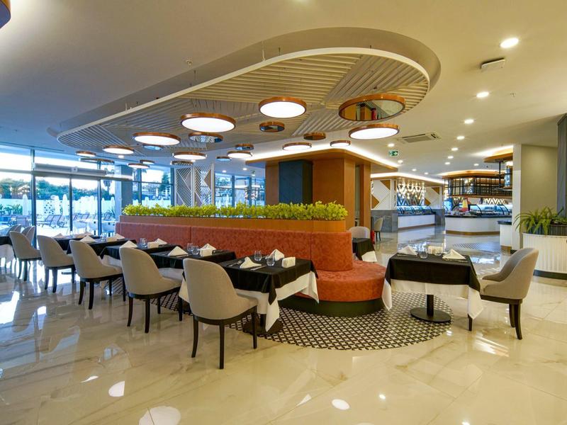 Ruime eetzaal in hotel met moderne stoelen, ronde tafels en decoratieve plafondverlichting.