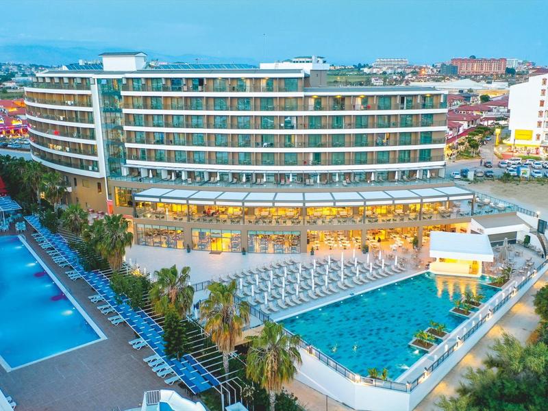 Modern hotel met grote zwembaden, palmbomen en ligstoelen nabij een kuststad.