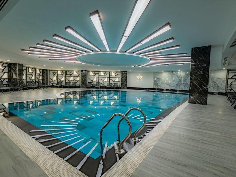 Binnenzwembad met moderne verlichting en betegelde vloer in een ruime wellnessruimte.
