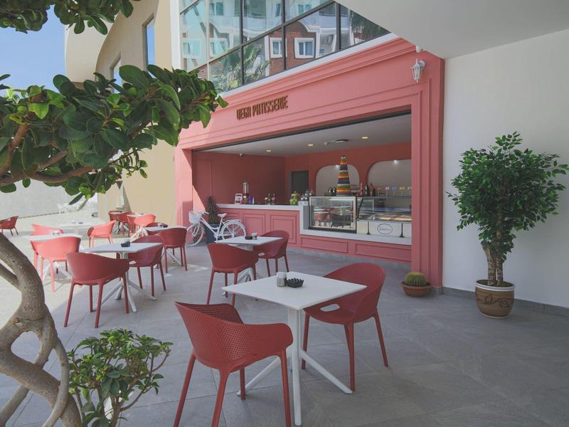 Buiten café met rood stoelen en tafels onder een moderne roze luifel.