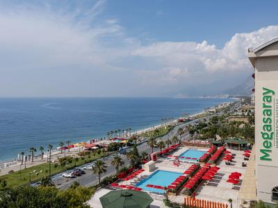 Terrazza dell'hotel con piscina, ombrelloni rossi e vista sulla spiaggia e sul mare.