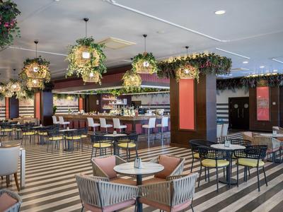 Moderní hotelová restaurace s dekorativními závěsnými květinami a pruhovanou podlahou.