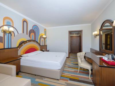 Ložnice s velkou postelí, barevným kobercem a dřevěným nábytkem v hotelovém pokoji.