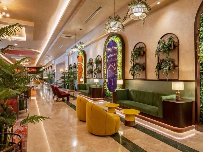 Elegantní hotelová lobby s rostlinami, žlutými křesly a stylovým osvětlením.