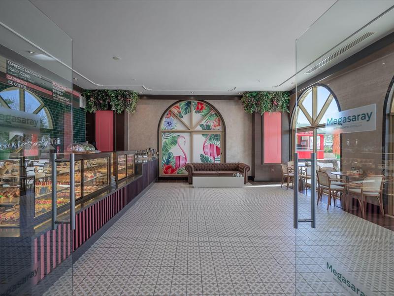 Moderní pekárna se skleněnými vitrínami, velkými okny a posezením s pohovkou.