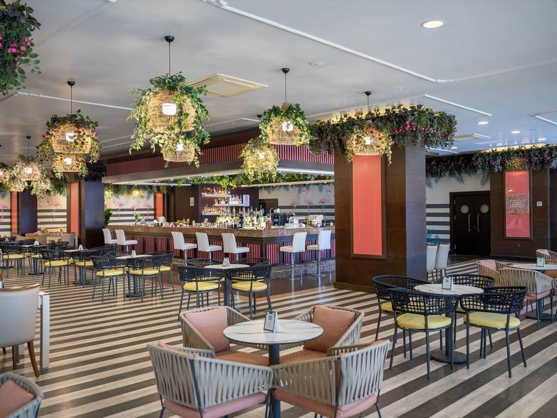 Moderní hotelová restaurace s dekorativními závěsnými květinami a pruhovanou podlahou.