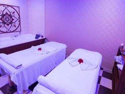 Zwei weiße Massageliegen mit Rosen in einem violett beleuchteten Behandlungsraum.
