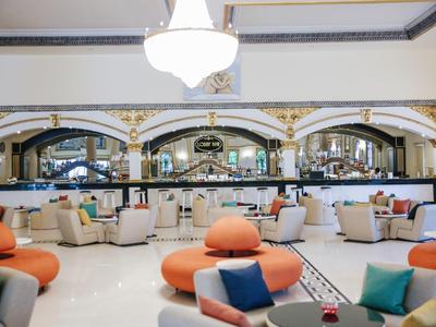 Großer, heller Raum mit modernen Sitzecken, weißen Sesseln und orangefarbenen Sofas.