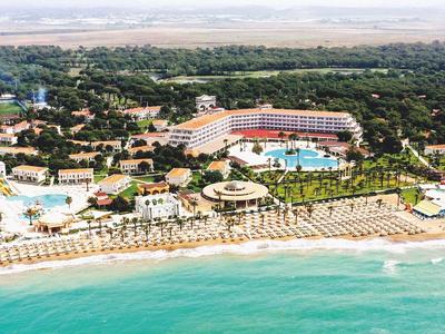 Große Hotelanlage mit Pools, Palmen und Strand an türkisfarbenem Meer unter klarem Himmel.