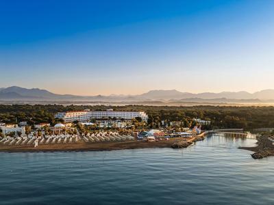 Strandresort met ligstoelen, bars en hutten aan kalme zee onder een heldere hemel.