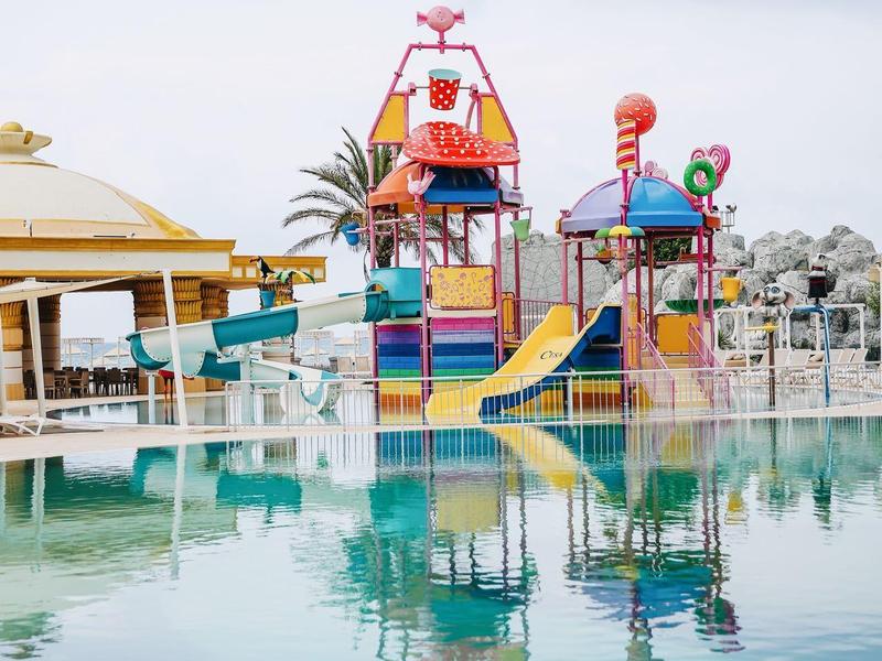 Kleurrijk waterspeelgebied met glijbanen en figuren bij het zwembad onder bewolkte lucht.
