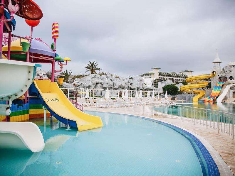 Kleurrijke waterspeeltuin en glijbanen bij een hotelzwembad onder een bewolkte hemel.