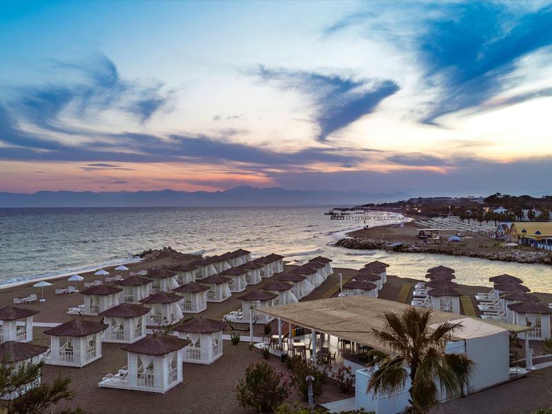 Strandresort met rijen witte strandhuisjes aan zee bij zonsondergang.