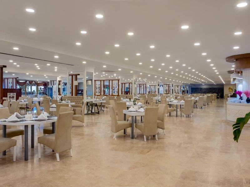 Grote, lichte eetzaal met gedekte tafels en comfortabele stoelen.