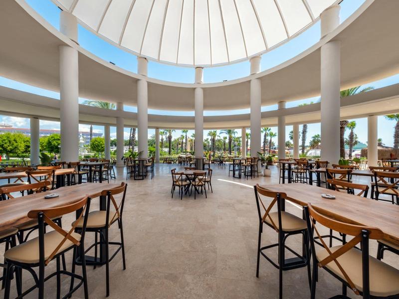 Grote lichte ruimte met houten tafels en stoelen onder een ronde glazen dak.