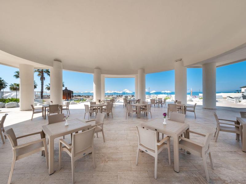 Overdekt buitenterras met tafels en stoelen met uitzicht op zee